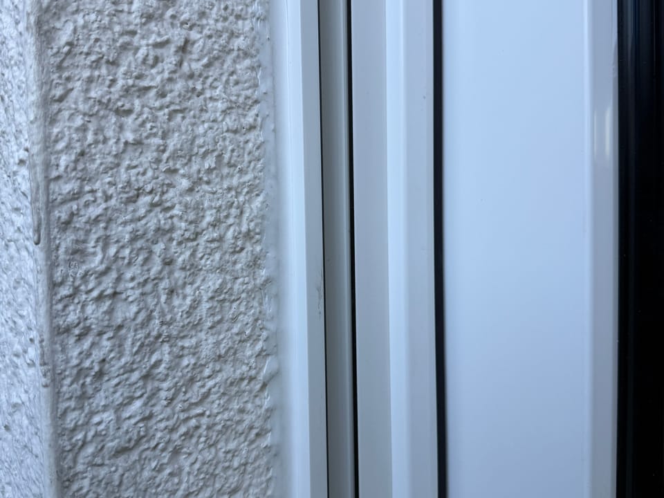 Seitlicher Anschluss eines neuen weißen Fensterrahmens an die verputzte Laibung