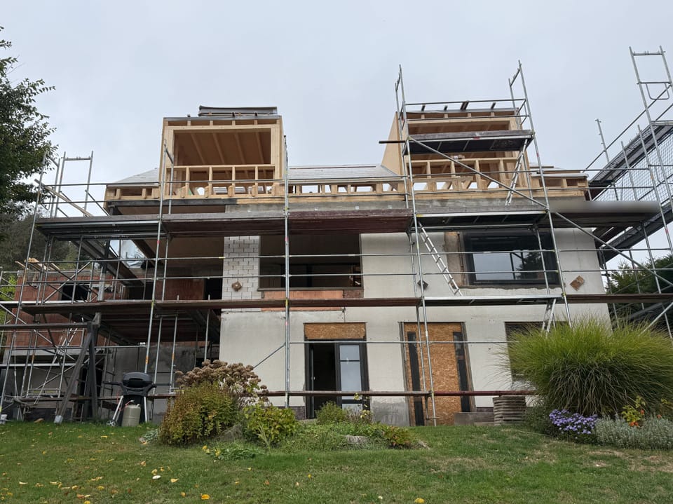 Das Haus im Gerüst von der Gartenseite, auf dem Dach zwei kastenförmige Aufbauten aus hellem Holz