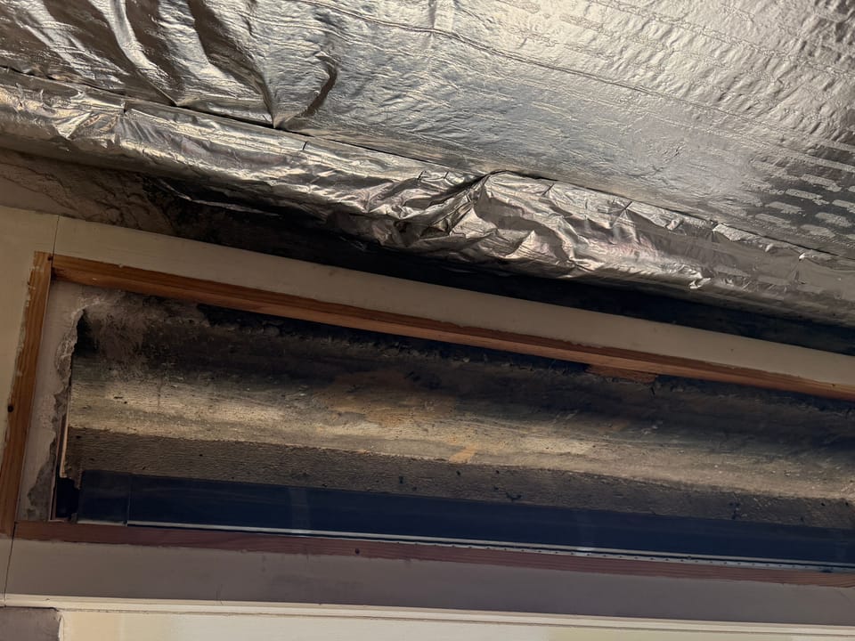 Geöffneter alter Rollladenkasten über einer Fensteröffnung, darüber Dämmfolie, nach dem Ausbau des alten Fensters