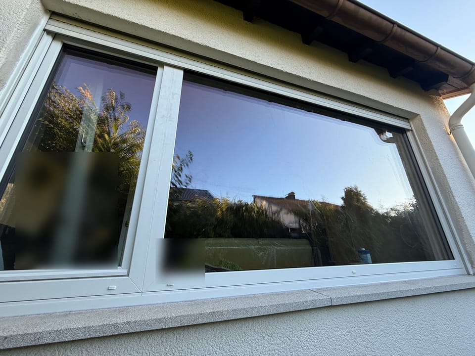 Großes zweiteiliges Fenster mit weißem Rahmen von außen, darüber der Rollladenkasten unter dem Dachüberstand